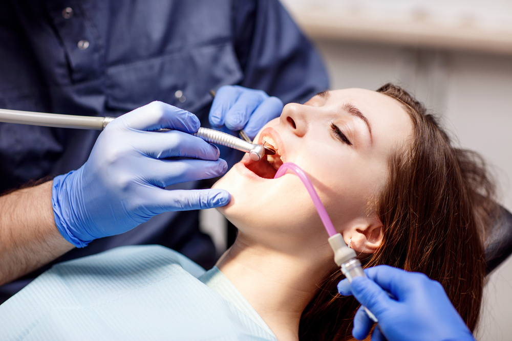 Male dentist treating teeth to young woman patient in clinic.
